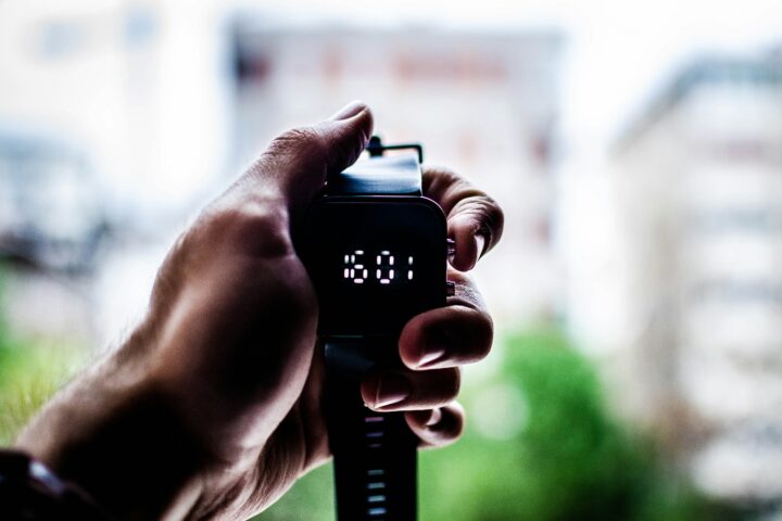 Close-up of a hand pressing the start button on a black digital stopwatch outdoors.
