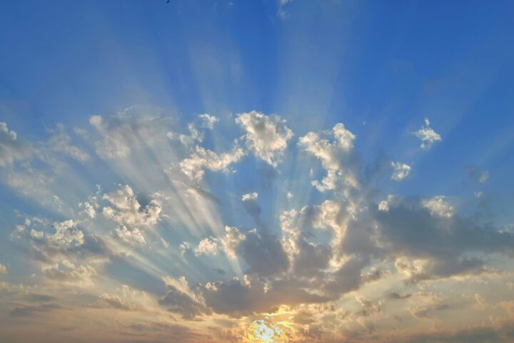 Sunset sky with golden light peeking through clouds and sunbeams extending upward from the horizon