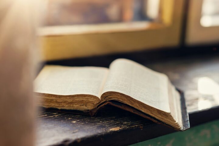 Open antique book on a dark wooden desk with warm light in the background, pages spread apart.