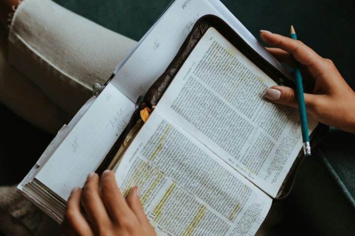 Open Bible with highlighted passages, a pencil held by a right hand ready to take notes.
